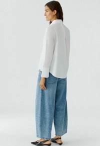 Witte blouse met lange mouwen en een klassieke kraag, gecombineerd met lichtblauwe denim jeans met een hoge taille en grote zakken.