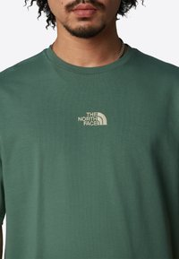 Camiseta de algodón verde con un pequeño logo bordado en beige de "The North Face" en el pecho. Cuello redondo y mangas cortas.