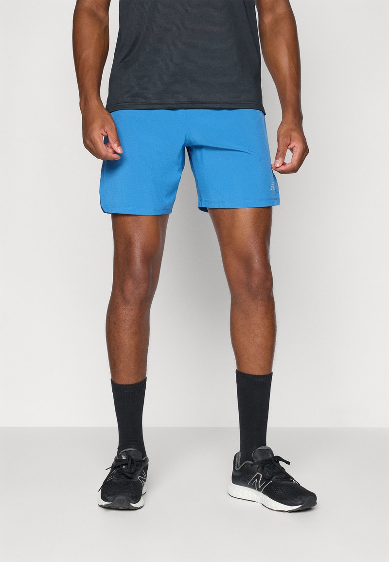 Blaue Sportshorts mit glatter Textur, die eine lockere Passform bieten. Kombiniert mit schwarzen Sportschuhen und schwarzen Crew-Socken.