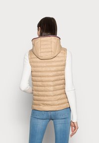 Beżowa kamizelka puchowa z kapturem, z poziomymi przeszyciami, kontrastową fioletową podszewką i gładką, błyszczącą teksturą.