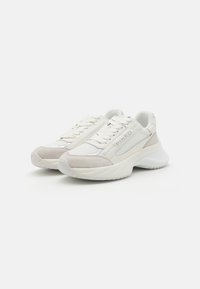 Sneaker bianche e beige chiaro realizzate in un mix di pelle e camoscio, con linguetta imbottita, suola testurizzata e un marchio ben visibile di lato.