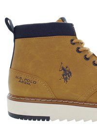 Scarpa alta tan U.S. Polo Assn. con collo alla caviglia navy, lacci beige e suola bianca con battistrada nera, che mostra il logo del marchio e dettagli di cucitura.