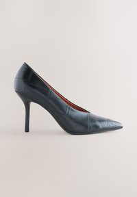 Escarpin en cuir noir à talons hauts avec bout pointu et détail de motif carré cousu, présenté de profil sur fond neutre.