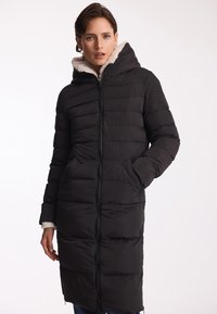 Czarna, ocieplana kurtka z zapięciem na zamek, kapturem i sztucznym futrem. Posiada skośne kieszenie oraz długi, prosty krój. Teksturowana tkanina.