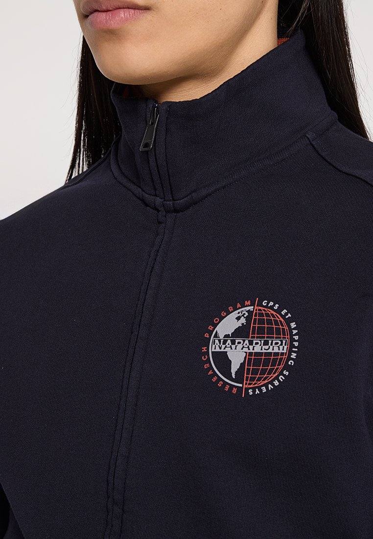 Marinblå zip-up jacka med hög krage, prydd med en röd jordglob logotyp och text. Tillverkad av mjukt tyg med en slät yta.