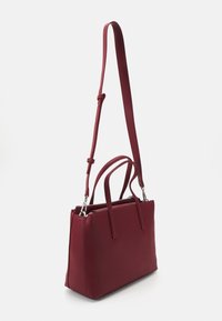 Burgundy käsilaukku, joka on valmistettu sileästä materiaalista. Siinä on kaksi ykköskahvaa, säädettävä olkahihna ja vetoketjukiinnitys.