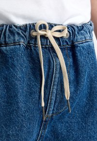 Denimshorts met een elastische tailleband en een beige koord. De stof is middentint blauw met een klassieke denimtextuur en stikdetails.