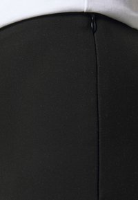 Černá úzká sukně vyrobená z texturované látky, která má decentní zip na zadní straně a hladký siluetu s čistými liniemi.