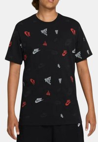 Maglietta nera con logo Nike ripetuto e testo "Just Do It" in rosso, bianco e grigio. Maniche corte, vestibilità casual, materiale in cotone.