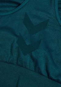 Sportowy biustonosz w kolorze morskim z dwoma ciemnymi wzorami w formie szewronów z przodu oraz szerokim prążkowanym pasem na dole.