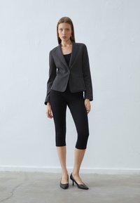 Szürke, szabott zakó, bemetszett hajtókával, testhezálló kialakítással, egy gombos záródással, fekete leggings-szel és magassarkú cipőkkel párosítva.