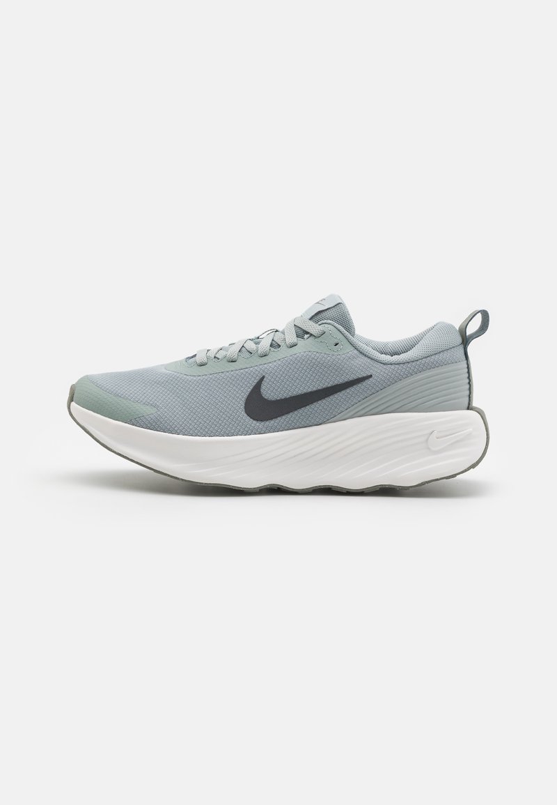 Baskets de sport gris clair avec tige en mesh, semelle blanche incurvée, lacets gris et logo Swoosh noir sur le côté. Présente un design texturé.