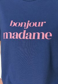 Navy blue t-paita, joka on valmistettu pehmeästä kankaasta ja jossa on vaaleanpunainen graafinen printti, jossa lukee "bonjour madame" modernilla fontilla.
