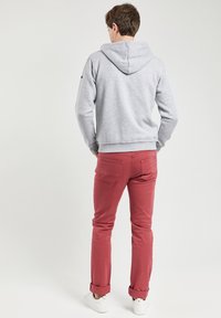 Sweat à capuche gris avec un cordon de serrage, associé à un jean bordeaux et des baskets blanches. Le sweat à capuche possède une poche kangourou et des poignets côtelés.