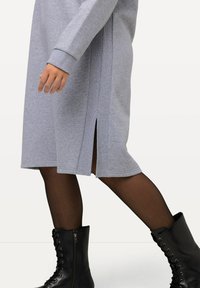 Vestido de algodón gris con mangas largas, de longitud media entre las pantorrillas, con aberturas laterales. Combinado con botas de tobillo negras con cordones.