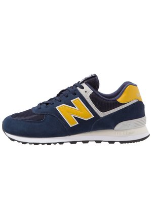 Chaussure de course bleu marine et jaune avec une tige en mesh et daim, logo jaune sur le côté, semelle blanche et semelle extérieure noire.