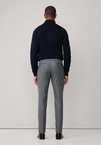 Mornarsko plava pletiva s visokim ovratnikom uparena sa svijetlosivim krojenim hlačama koje imaju stražnje džepove i metalne gumbe.