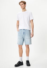 Lyseblå denimshorts med to store forlommer, parret med en ensfarvet hvid t-shirt med korte ærmer og sorte sko.