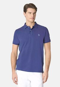 Polo shirt viola semplice con una pattina a tre bottoni e maniche corte. Presenta un piccolo logo blu sul lato sinistro del petto. Tessuto in cotone morbido.