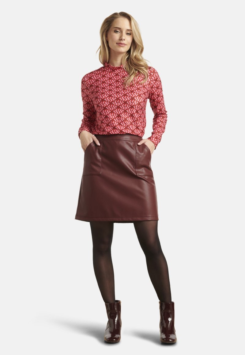 Rode, met een patroon, langemouwen top gecombineerd met een bordeaux faux leren rok met zijzakken, gedragen met zwarte panty's en glanzende enkellaarsjes.