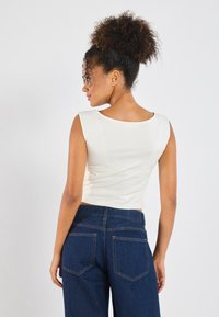 Top recortado sin mangas en tela color blanco roto con escote redondo, combinado con jeans oscuros de tiro alto con costuras en contraste.