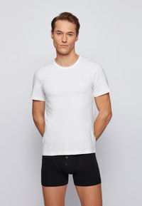 Witte katoenen T-shirt met korte mouwen en ronde halslijn, gecombineerd met zwarte aansluitende boxershorts met knoopdetails.