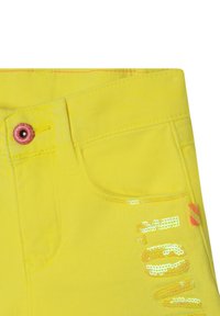 Žluté džíny šortky s přední kapsou, růžovým knoflíkem a detaily z flitrů na bocích se zigzagovým vzorem v oranžových akcenty.