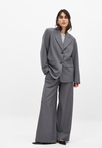 Pelēku svītrainu uzvalku, kas sastāv no brīva žaketes ar izgriezumu un platām biksēm. Gluda tekstūra un divu pogu aizdare.