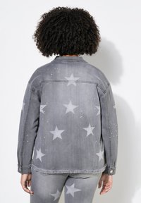 Grå denimjacka med stjärnmönster och nitar, med fransad nederkant och knäppningar vid ärmsluten. Strukturerad väv med en avslappnad passform.