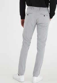Grå skräddarsydda byxor med en subtil textur, smal passform, två bakfickor med knappar och bälteshällor, i kombination med vita sneakers.