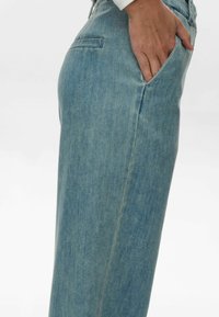 Világoskék farmernadrág egyenes szárú dizájnnal, oldalsó zsebekkel és diszkrét textúrával. Testre szabott szabás és klasszikus stílus.