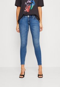 Vaqueros ajustados de mezclilla azules, con un diseño clásico de cinco bolsillos, cintura de altura media y un ligero desgastado. Combinados con una camiseta gráfica negra.