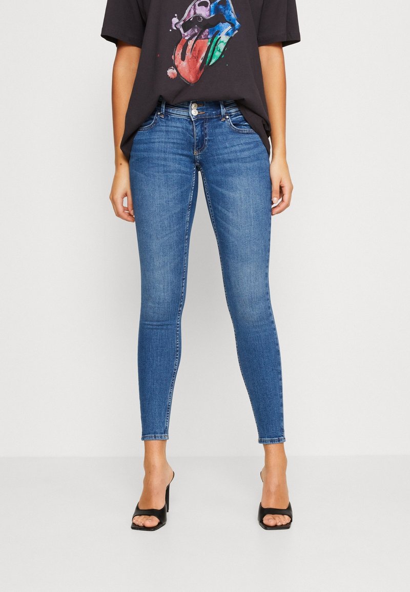 Vaqueros ajustados de mezclilla azules, con un diseño clásico de cinco bolsillos, cintura de altura media y un ligero desgastado. Combinados con una camiseta gráfica negra.
