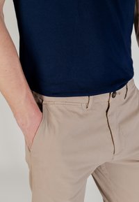 T-shirt di cotone blu marina abbinata a pantaloni beige. I pantaloni presentano una tasca frontale, chiusura con bottone e una texture di tessuto liscia.