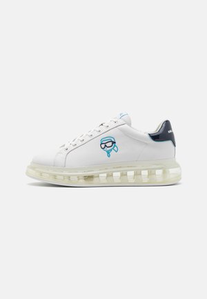 Hvid sneaker med gennemsigtig tyk sål, blå og sort logo på siden, sort hælkappe og hvide snørebånd vist fra højre side.