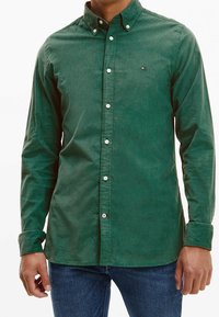 Camisa verde con botones, confeccionada en tela texturizada, con cuello abierto, botones delanteros y un pequeño logo en el pecho.