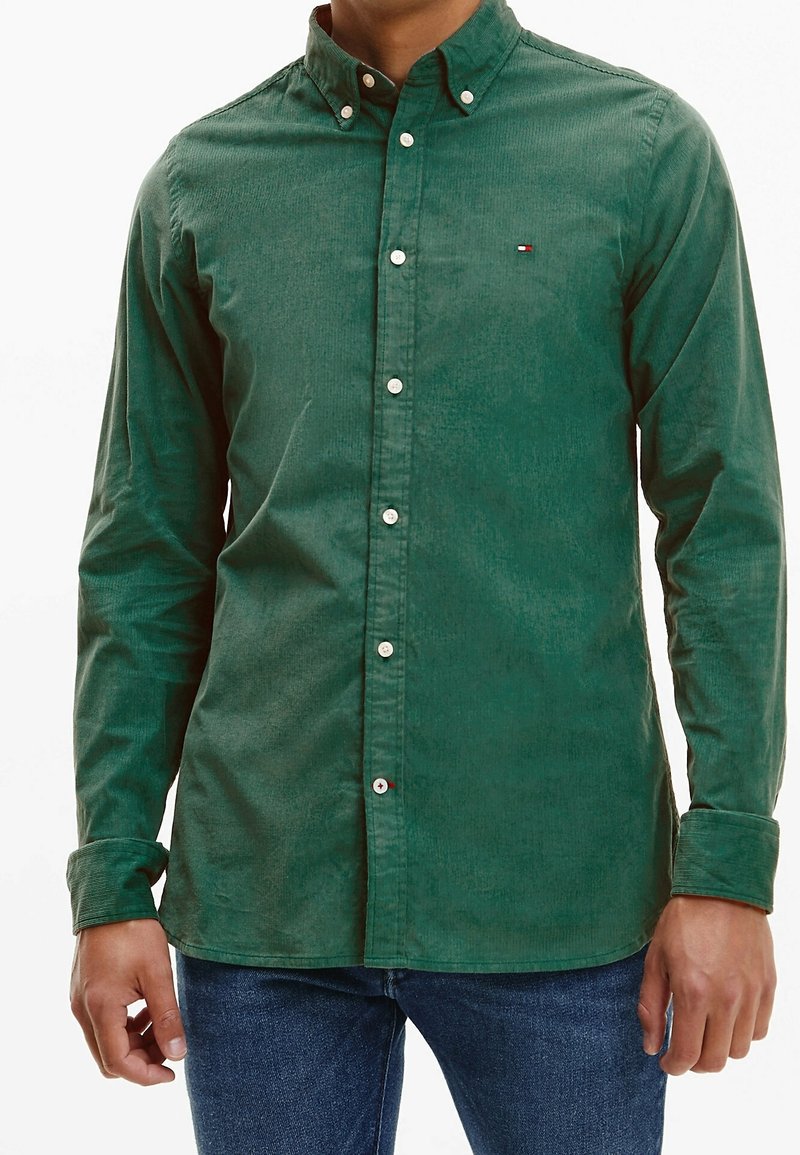 Camisa verde con botones, confeccionada en tela texturizada, con cuello abierto, botones delanteros y un pequeño logo en el pecho.
