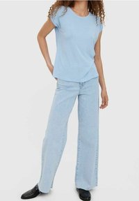 Jasnoniebieska koszulka z krótkim rękawem i okrągłym dekoltem, zestawiona z jasnoniebieskimi, szerokimi spodniami o wysokim stanie oraz czarnym obuwiem.