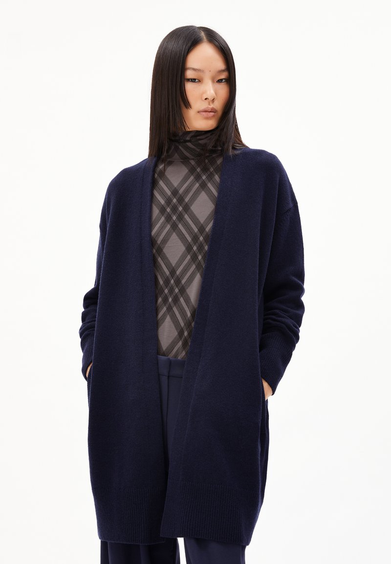 Langer marineblauer Cardigan aus einem weichen Strickmaterial, mit offenem Vorderteil, oversized Ärmeln und zwei Seitentaschen. Texturierte, gerippte Bündchen.