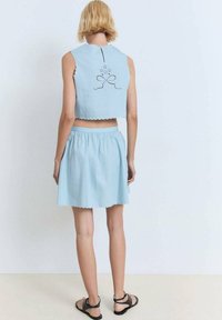 Top corto azul claro con bordes festoneados y detalle de lazo de ojales en la parte posterior, combinado con una falda acampanada a juego con cintura elástica.