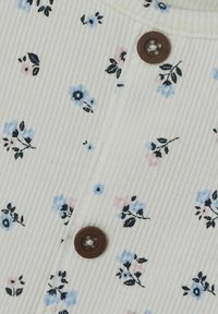 Weißer gerippter Stoff mit kleinen blauen, rosa und schwarzen Blumenmotiven. Brauner Knopfakzent im Kragenbereich. Weiche Textur.