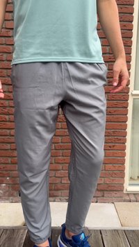 Pantaloni sportivi grigi con vita elastica e tasche laterali, realizzati in tessuto leggero e liscio; abbinati a scarpe da ginnastica blu.