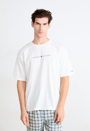 Weißes Baumwoll-T-Shirt mit kurzen Ärmeln, mit einem zentralen „TOMMY HILFIGER“-Logo in Blau und Rot. Schlichtes Design, lockere Passform.