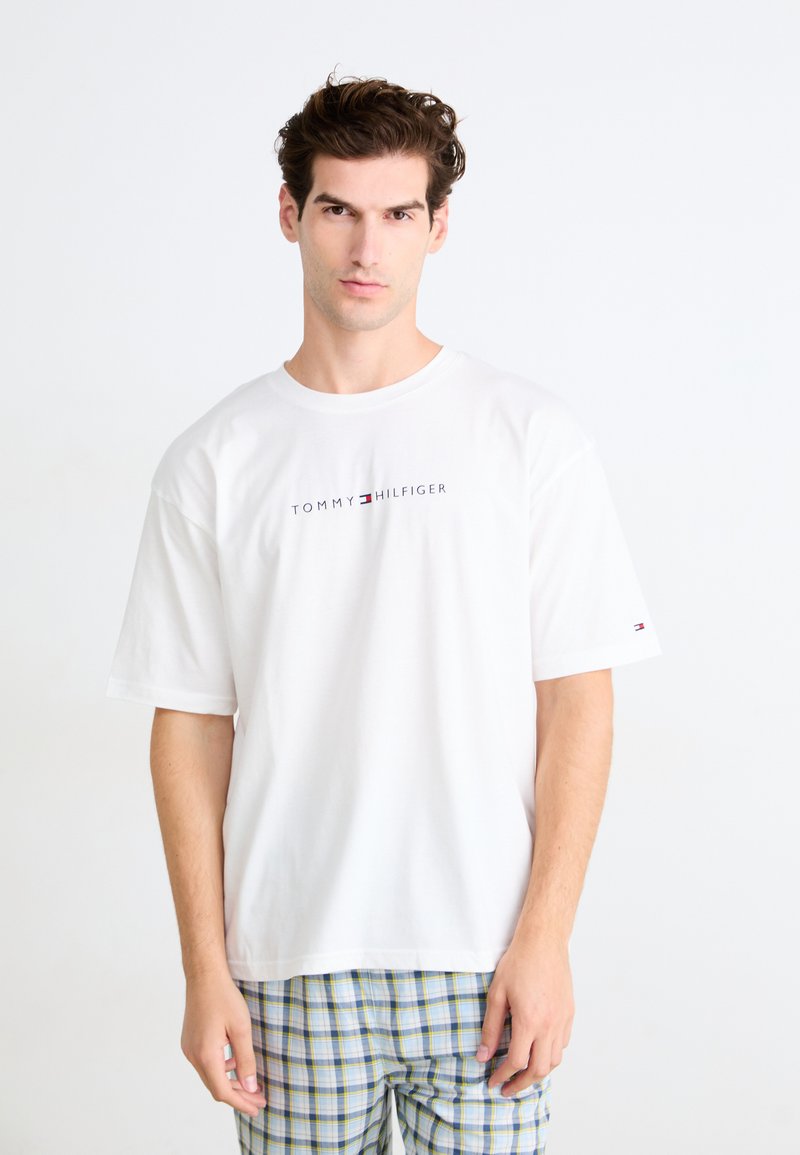 Bjela pamučna majica kratkih rukava s centralnim "TOMMY HILFIGER" logotipom u plavoj i Crvenoj boji. Jednostavan dizajn, opušteni kroj.
