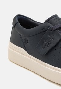 Marinblå lædersneaker med perforerede side detaljer, rund tå og hvid gummisål. Har et mærke-tag og matchende snørebånd.