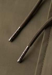 Olivově zelená látka se dvěma tmavě hnědými texturovanými šnůrami a kovovými koncovkami s rytinou "onude". Hladký povrch a minimalistický design.