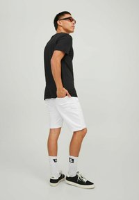 Camiseta negra de manga corta, shorts blancos enrollados, zapatillas negras, calcetas blancas y gafas de sol. El conjunto presenta un ajuste casual y cómodo.