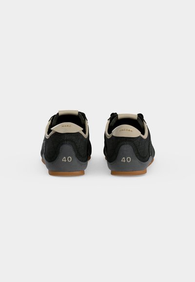 Paire de baskets basses noires avec languettes beiges portant les mentions "Marc" et "Jacobs,", taille 40, vues de dos sur un fond uni.