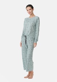 Vaaleansininen pyjamapuku, jossa on pitkät hihat ja löysät housut. Sisältää pieniä kukkakuosisia yksityiskohtia, naru vyötäröllä ja pehmeä kangas.