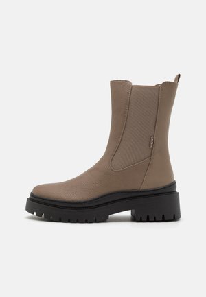 Tan chelsea boots with a textured leather finish, elastic sides, and a chunky black rubber sole featuring a rugged tread pattern.